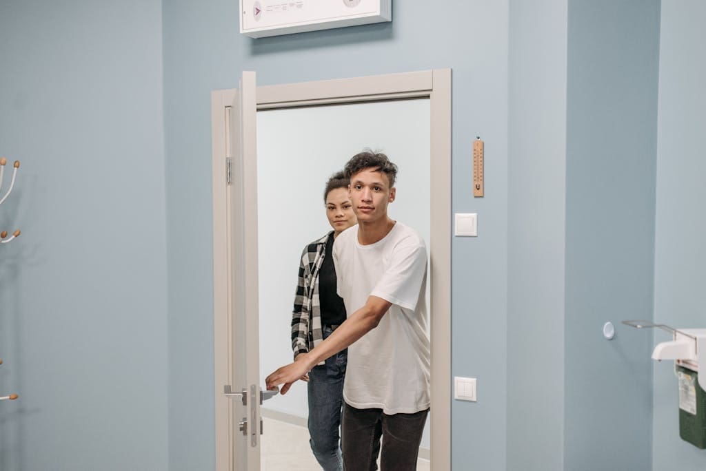 A young couple stepping through a modern doorway into a well-lit room with a light blue wall.