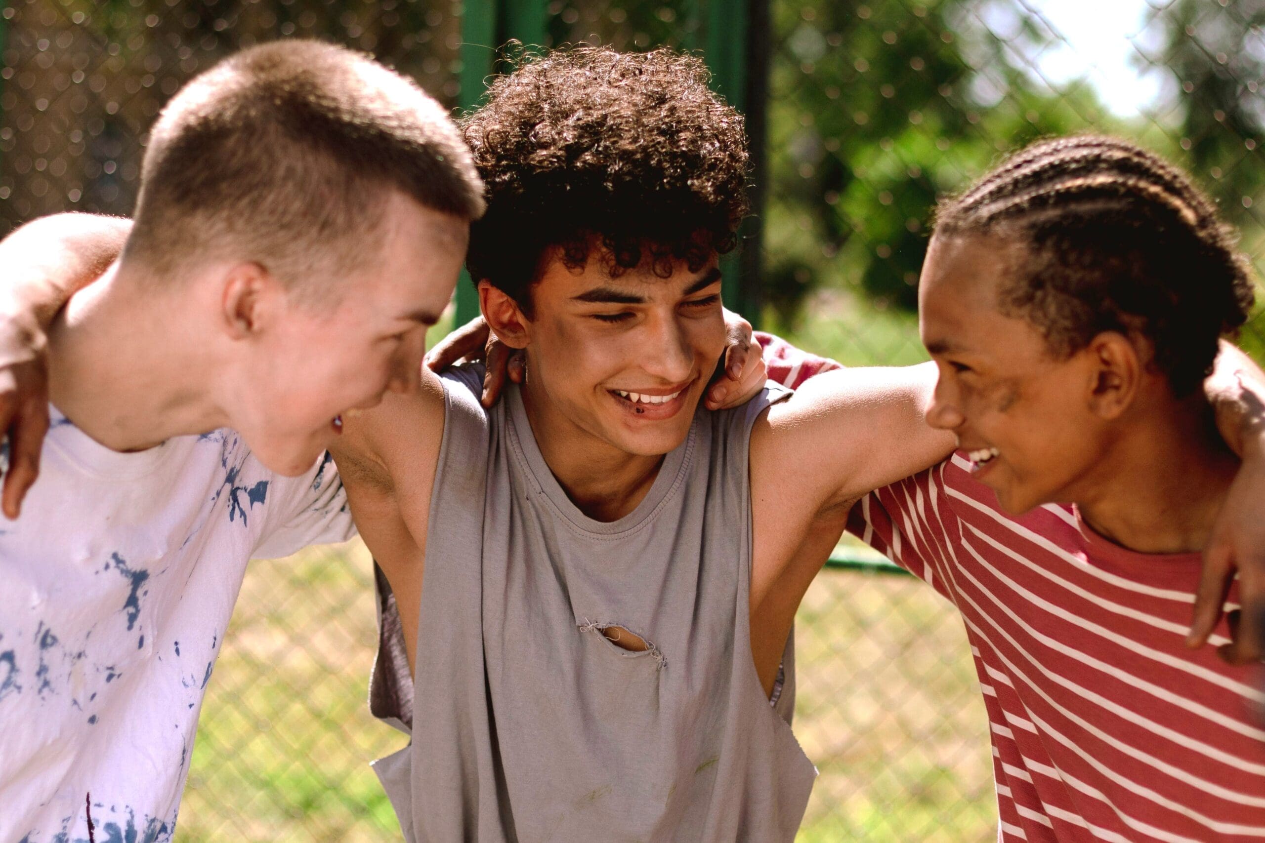 Three male friends smiling with their arms around each others shoulders.