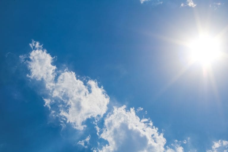 A clear blue sky with fluffy clouds and bright sunshine, representing a perfect summer day. Don't let heat-related illness get in the way!