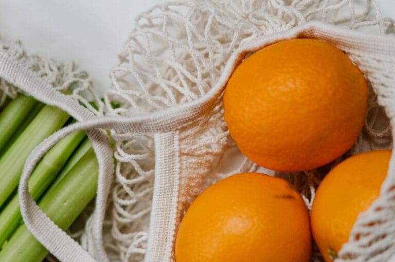 Mesh bags containing fresh oranges and celery stalks.