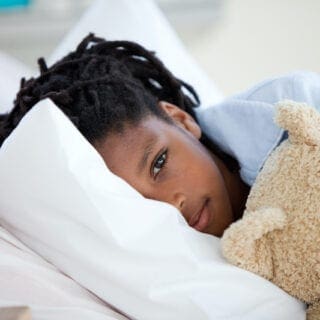 Child laying in bed with teddy bear for comfort