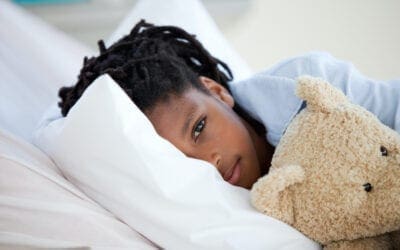 Child laying in bed with teddy bear for comfort