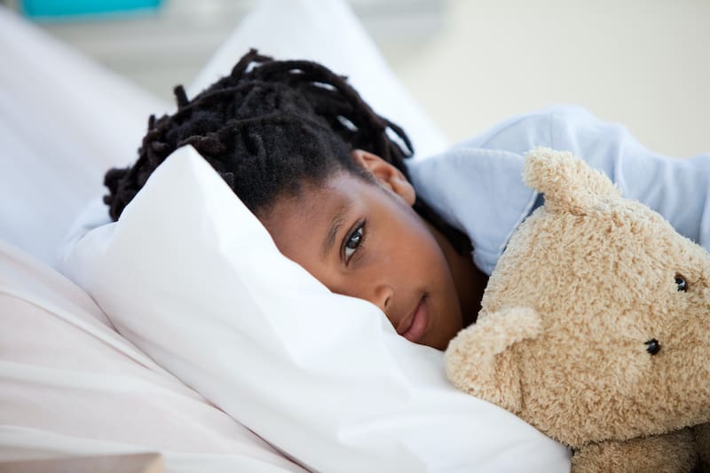 Child laying in bed with teddy bear for comfort