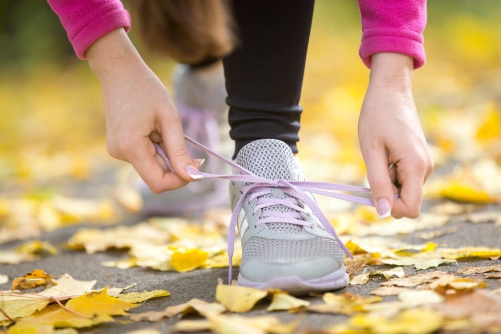 Hands tying tennis shoes. The asphalt is covered in fall leaves.