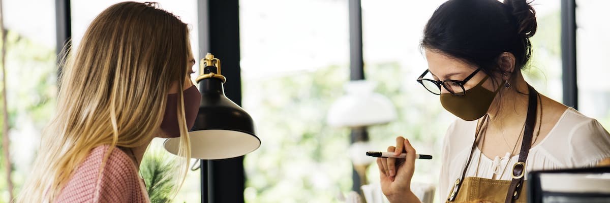 Woman wearing mask ordering food in a cafe restaurant covid 19