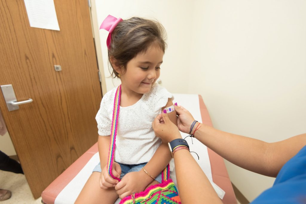 A healthcare provider puts a band-aid on a young girl's bicep