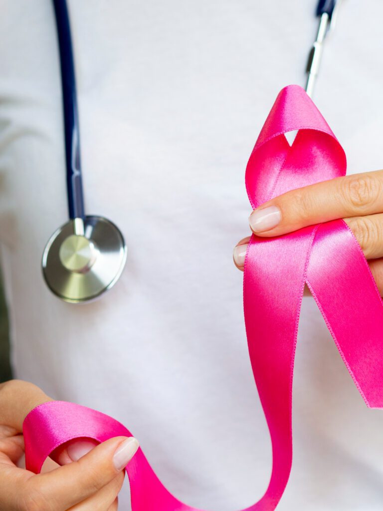 A healthcare provider holding a pink breast cancer ribbon.