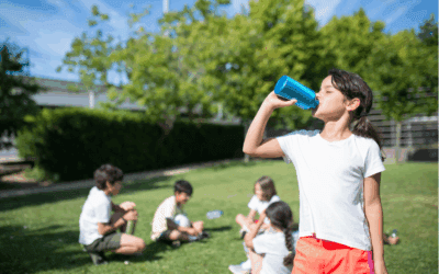 Following cool tips for a healthy summer, a girl drinks from a water bottle in front of friends who are taking a break from playing soccer outside.