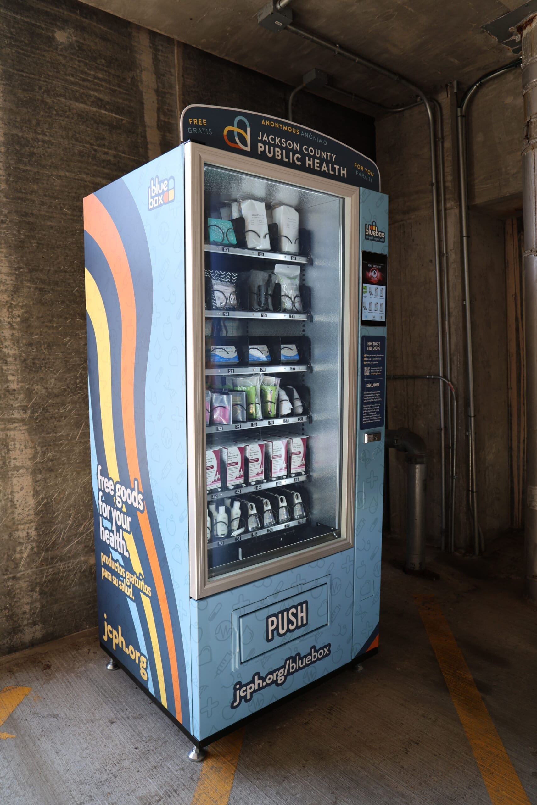 The images shows a bluebox self-serve vending machine that's stocked with free health items including naloxone nasal spray, safe sex products, first aid kits, and more.
