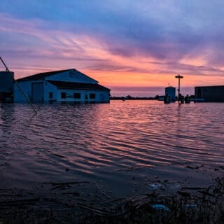 Photo of Levasy Flood in 2019 by Matt Evans. Flooding overwhelms a house at sunset; Spring severe weather in Missouri can be devastating.