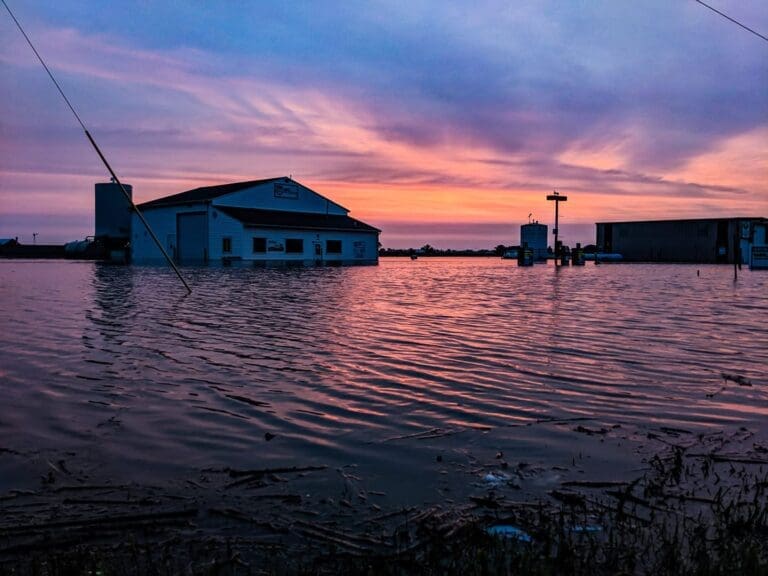 The sun sets over a flooded home in Levasy, Missouri. The water stretches across the horizon, with no ground in sight.