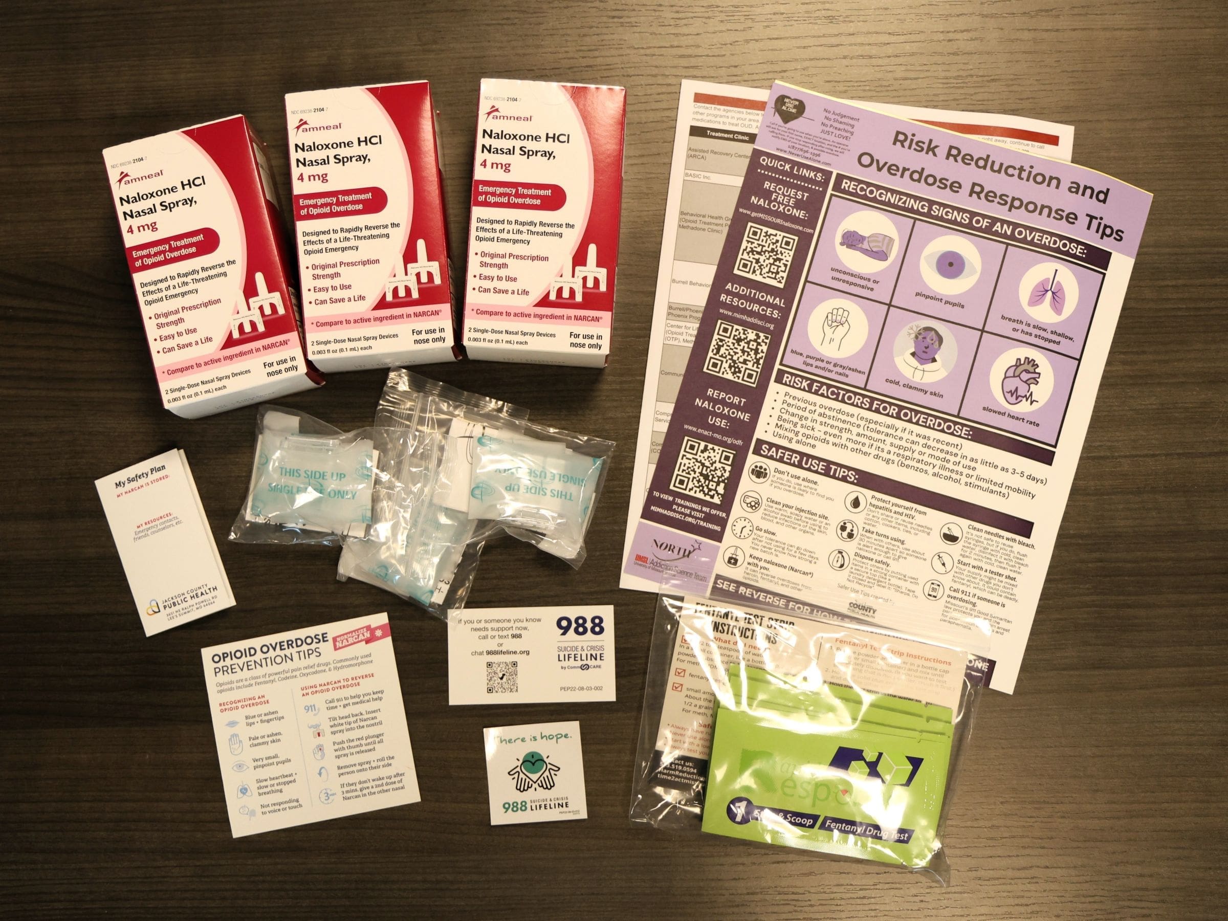 The images shows a variety of opioid overdose and awareness products including naloxone nasal spray, fentanyl test strips with instructions, CPR face masks, and various overdose response literature.
