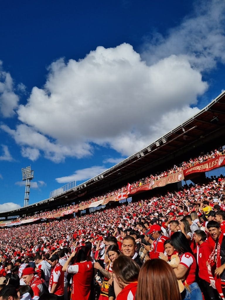 A lively crowd fills the Bogotá stadium under a vibrant blue sky.